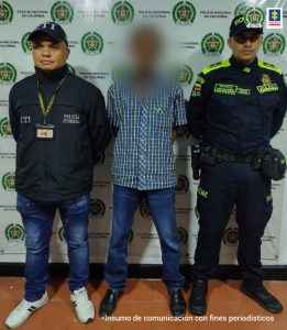 En la foto se aprecia de pie y con los brazos atrás a José Javier Gutiérrez Ramos. Viste con camisa de manga corta estampada con cuadros grises y rayas amarillas, verdes y blancas; jean azul y zapatos negros de material. Al lado derecho de él hay un servidor del CTI de la Fiscalía y al lado izquierdo un uniformado de la Policía Nacional. Detrás de ellos hay un pendón institucional de la Policía.