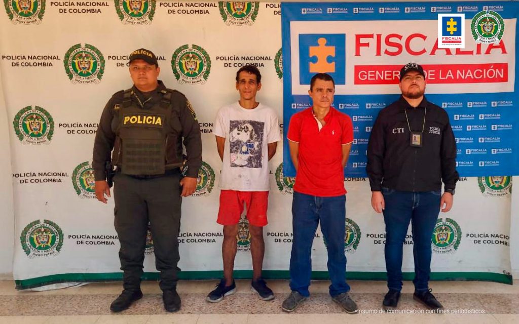 En la fotografía aparece un capturado junto a personal de Fiscalía General de la Nación y Policía Nacional. En la parte posterior de la imagen se ven banners de Policía Nacional y la Fiscalía General de la Nación.
