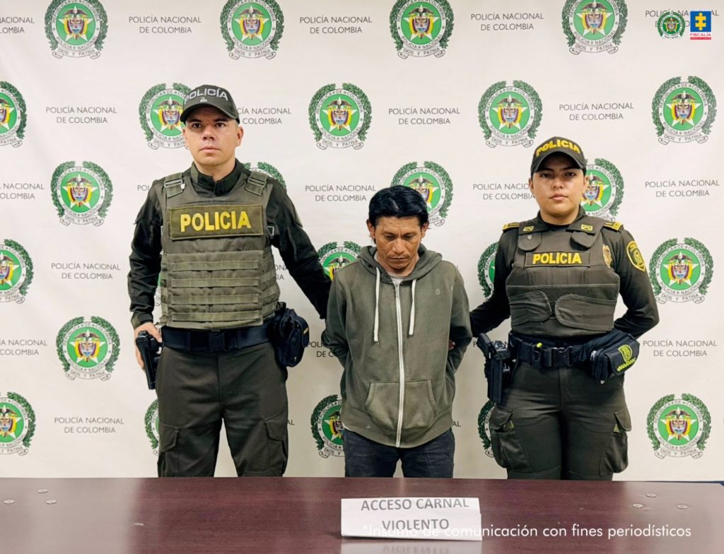 En la fotografía se aprecia de pie y con los brazos atrás a José Ortiz. Viste con buso de color verde oliva y pantalón negro. A sus extremos hay uniformados de la Policía Nacional. Delante de ellos hay una superficie de color marrón y sobre ella un letrero que dice: ‘Acceso carnal violento’. Detrás de ellos hay un pendón institucional de la Policía.