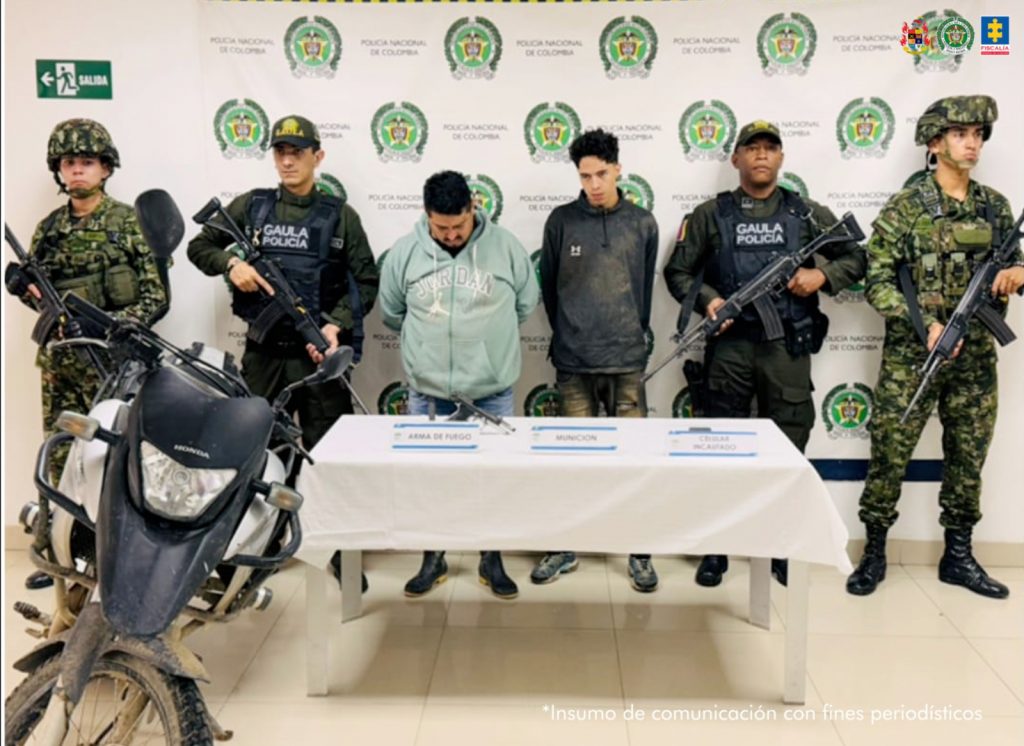 En la fotografía se aprecian de pie y con los brazos atrás a José Osvelio Arboleda Castro y Sebastián Gaviria Cárdenas. Uno viste chaqueta azul clara, jean azul y zapatillas negras. El otro usa chaqueta negra, pantalón gris oscuro desgastado. A los extremos hay uniformados de la Policía y Ejército Nacional. Delante de ellos hay una mesa con mantel blanco y sobre ella hay un arma de fuego, munición y un celular. Al extremo izquierdo de la fotografía hay una motocicleta. Detrás de los judicializados hay un pendón institucional de la Policía.