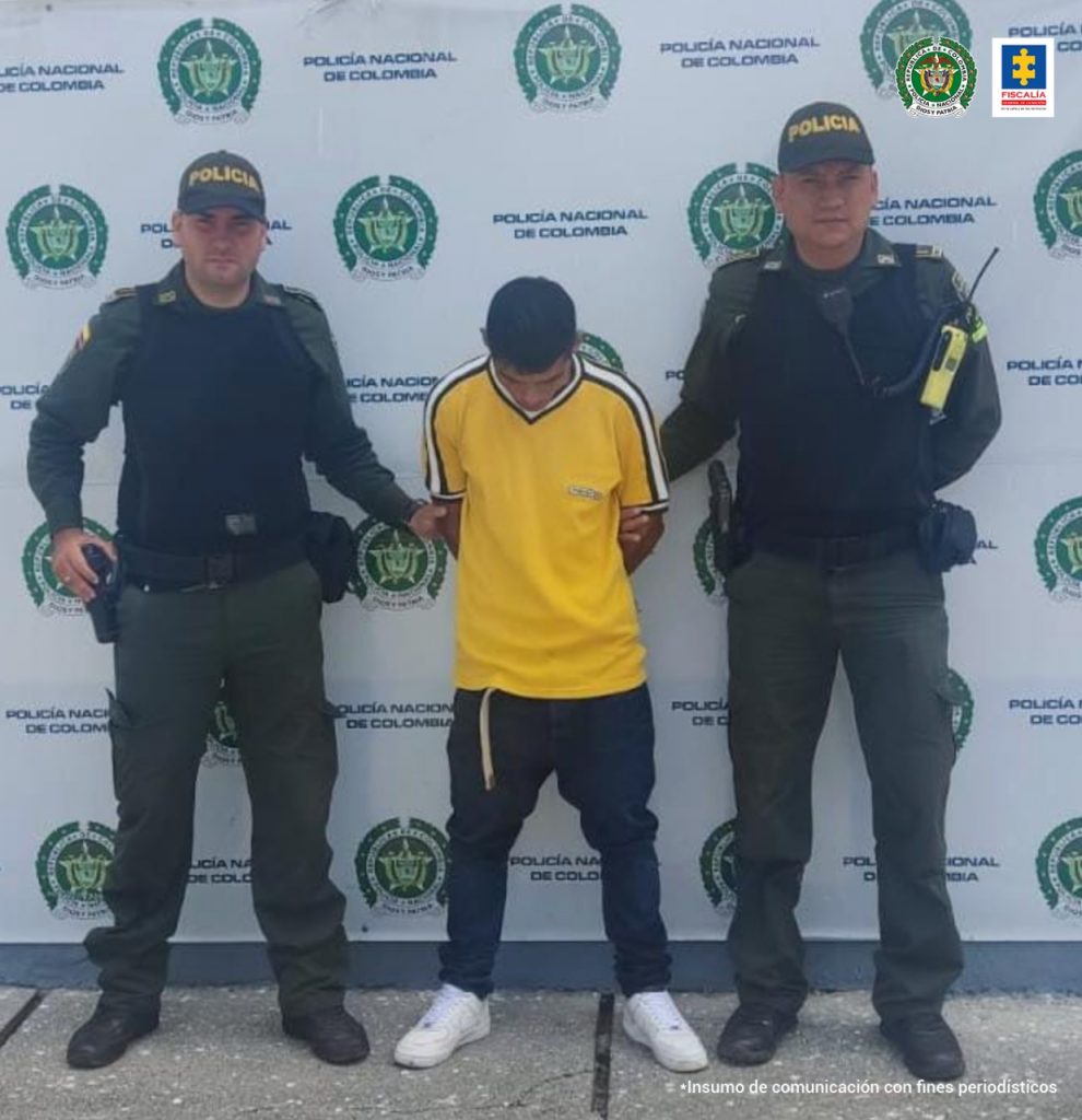 En la foto aparece, de pie, José Wilder Zúñiga, con los brazos atrás. Viste camiseta amarilla, pantalón oscuro y zapatillas blancas. A lado y lado de él hay uniformados de la Policía Nacional. Detrás de ellos hay un pendón institucional de la Policía.