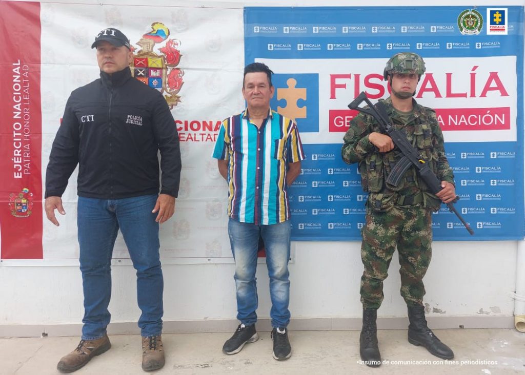 En la fotografía aparece un capturado, junto a personal de Fiscalía General de la Nación y Ejército Nacional. En la parte posterior de la imagen se ven banners de Ejército Nacional y la Fiscalía General de la Nación.