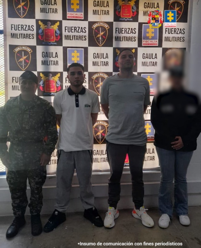 En la imagen están los dos procesados en medio de un servidor del CTI y otro del Ejército Nacional, y atrás hay un pendón con los logos de la Fiscalía General de la Nación, el Ejército Nacional y el Gaula militar 