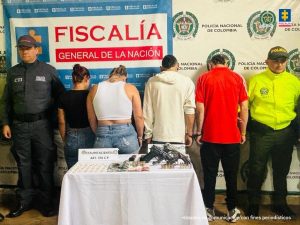  se observan cuatro capturadas en fila y de espaldas.  A cada costado funcionarios del CTI, y Policía Nacional. Al frente una mesa con material incautado.  Atrás un pendón de la Fiscalía General de la Nación y otro de Policía Nacional