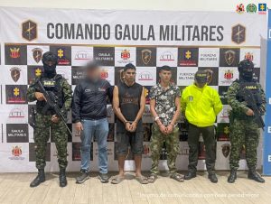 En la fotografía aparecen de pie, con los brazos adelante y esposados Juan Carlos Corrales Hincapié y Jhon Breyner Bernal González. Uno, viste con camiseta sin mangas, de color negro y estampado marrón a la altura del pecho; bermuda de color verde oscuro y pantuflas verdes. El otro viste camisa y pantalón camuflados y pantuflas verdes. Al extremo derecho hay un servidor del CTI de la Fiscalía y un uniformado del Ejército. Al extremo derecho hay un uniformado de la Policía Nacional y del Ejército. Detrás de ellos hay dos pendones institucionales de la Fiscalía y del Ejército.