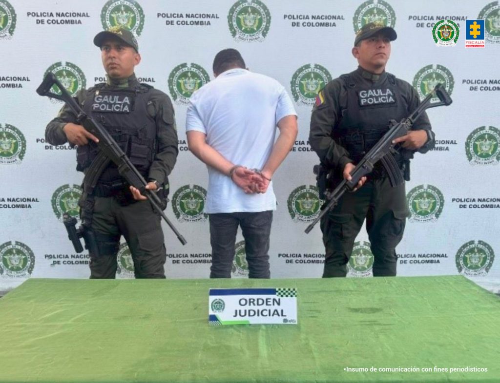 En la fotografía aparece de espaldas a la cámara, con la cabeza inclinada hacia adelante, los brazos atrás y esposado Juan Carlos Salgado Sánchez. Viste con camisa de color blanco, mangas cortas y pantalón gris oscuro. En sus extremos hay uniformados de la Policía Nacional. Delante hay una superficie de color verde oliva y sobre ella hay un letrero con el escudo de la Policía que dice: ‘Orden judicial’. En la parte posterior hay un pendón institucional de la  Policía.