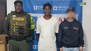En la fotografía aparece de pie y con los brazos atrás Juan Carlos Urbano Riascos. La fotografía fue tomada cuando se materializó la captura. Viste camiseta de manga corta, de color blanco; pantaloneta verde y pantuflas grises. Al extremo izquierdo hay un servidor del CTI de la Fiscalía y al lado derecho hay un uniformado de la Policía Nacional. Detrás de ellos hay un pendón institucional de la Fiscalía.