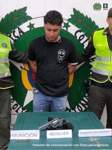 En la foto aparece Juan Daniel Isaza Osorio con los brazos atrás; vestido con camiseta negra y jean azul. Delante de él hay una mesa verde y sobre ella un arma de fuego, tipo revólver. A sus lados se aprecia a dos uniformados de la Policía Nacional. Detrás de ellos hay un pendón institucional de la Policía.