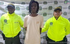 Juan David Asprilla Hurtado, de 23 años, en la foto con dos funcionarios de la Policia Nacional y de fondo el pendón con logos de la Policía.