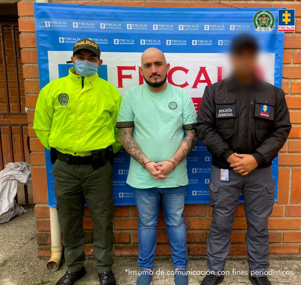 En la fotografía está el procesado con un uniformado de la Policía Nacional y una servirdora del CTI con un pendón azul de la Fiscalía