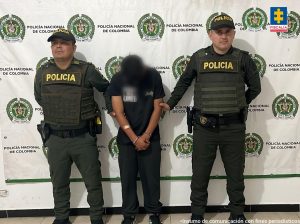 El procesado se encuentra esposado y en custodia por uniformados de la Policía Nacional. Detrás suyo un backing de la Policía.