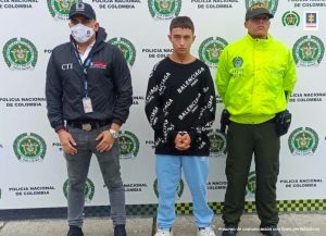 En la foto aparece de pie Juan Diego Zuluaga Naranjo, alias Lápiz. Viste buzo con estampados blancos, jean azul y zapatillas blancas. Al lado derecho de él hay un servidor del CTI de la Fiscalía, y al lado izquierdo un uniformado de la Policía Nacional. Detrás de ellos hay un pendón institucional de la Policía.