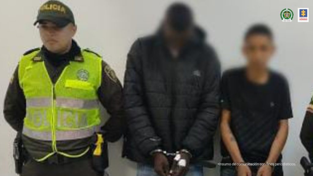 Capturados de frente esposados, custodiados por uniformados de la Policía. Detrás banner de la Policía Nacional.