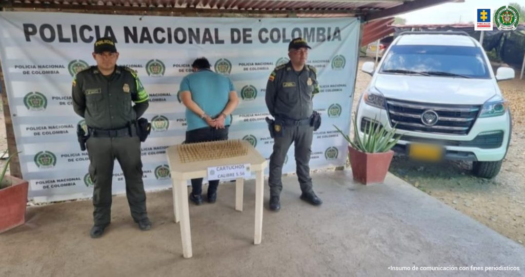 En la fotografía aparece un hombre capturado, acompañado de dos uniformados de la Policía Nacional. En la parte posterior dos banners con logos de la entidad.  