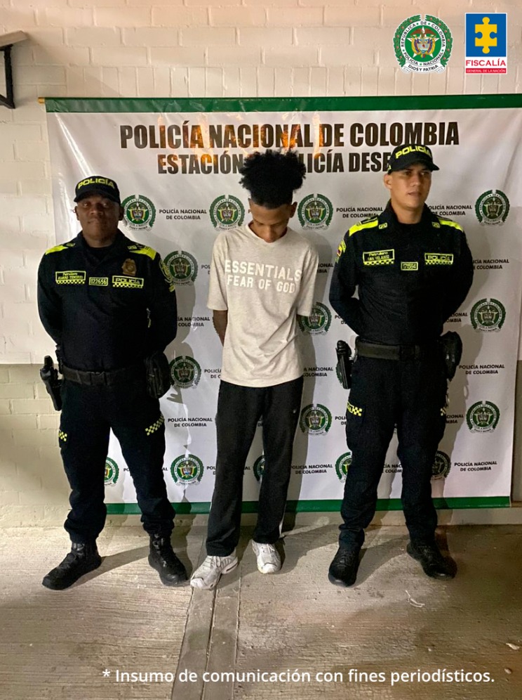 En la fotografía se aprecia de pie y con los brazos atrás a Juan José Pereira Zúñiga. Viste camiseta de manga corta color beige, pantalón negro y zaptillas blancas. A lado y lado de él hay uniformados de la Policía Nacional. Detrás de ellos hay un pendón institucional de la Policía.