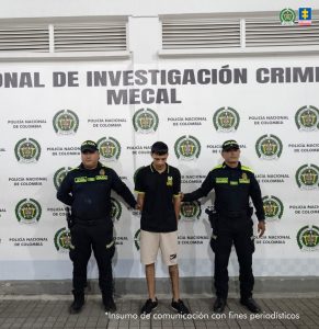 En la fotografía se aprecia de pie y con los brazos atrás a Juan José Ramos Osorio. Viste camiseta de color negro, mangas cortas, con ribetes de color verde limón en cuello y mangas; bermuda de color beage y zapatillas negras con blanco. A sus extremos hay uniformados de la Policía Nacional. Detrás de ellos hay un pendón institucional de la Policía.