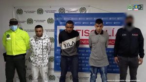 Se observan tres hombres de frente en fila, a un costado un funcionario del Cuerpo Técnico de Investigación CTI y al otro uno de Policía Nacional. Atrás un pendón de Fiscalía General de la Nación y otro de Policía Nacional