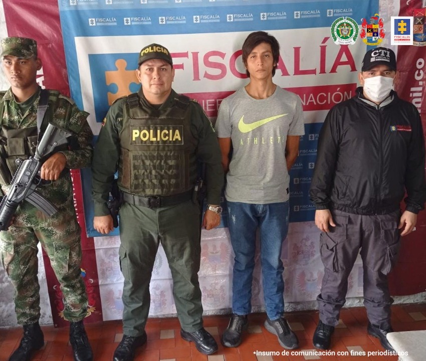 En la fotografía aparece un capturado, junto a personal de Fiscalía General de La Nación, Policía Nacional y Ejército Nacional. En la parte posterior de la imagen se ven banners de Policía Nacional, Ejército Nacional y Fiscalía General de la Nación.