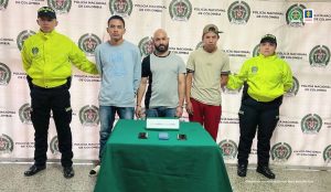  En la imagen están los 3 procesados con dos servidores de la Policía Nacional a los lados y una mesa al frente con los celulares incautados.