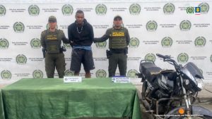 En la fotografía se aprecia de pie y con los brazos atrás a Juan Sebastián Mancilla León. Viste con buso de color negro, camisa por debajo de color azul; así como bermuda gris. A sus extremos hay uniformados de la Policía Nacional. Delante de ellos hay una mesa con mantel verde y sobre ella hay dos letreros que dicen: ‘Capturado Hurto’ y ‘Motocicleta recuperada’. En el extremo derecho de la fotografía hay una motocicleta. Detrás de ellos hay un pendón institucional de la Policía.