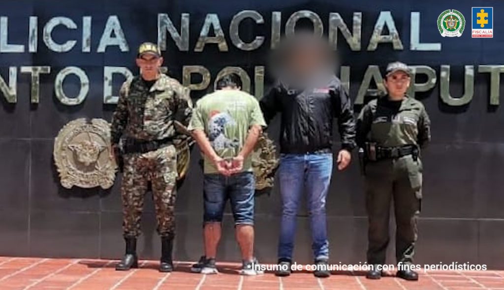 En la fotografía aparece una persona capturada en compañía de un uniformado de la Policía Nacional. En la parte posterior un banner con logos de la entidad. 