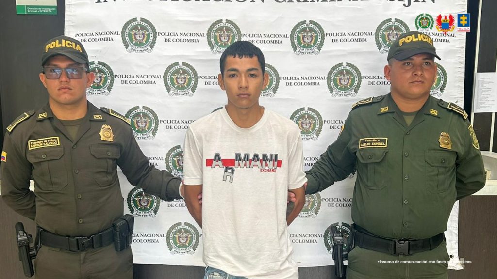 Se visualiza al capturado junto a dos uniformados de la Policía Nacional. Detrás de ellos el banner que identificara la Policía Nacional.