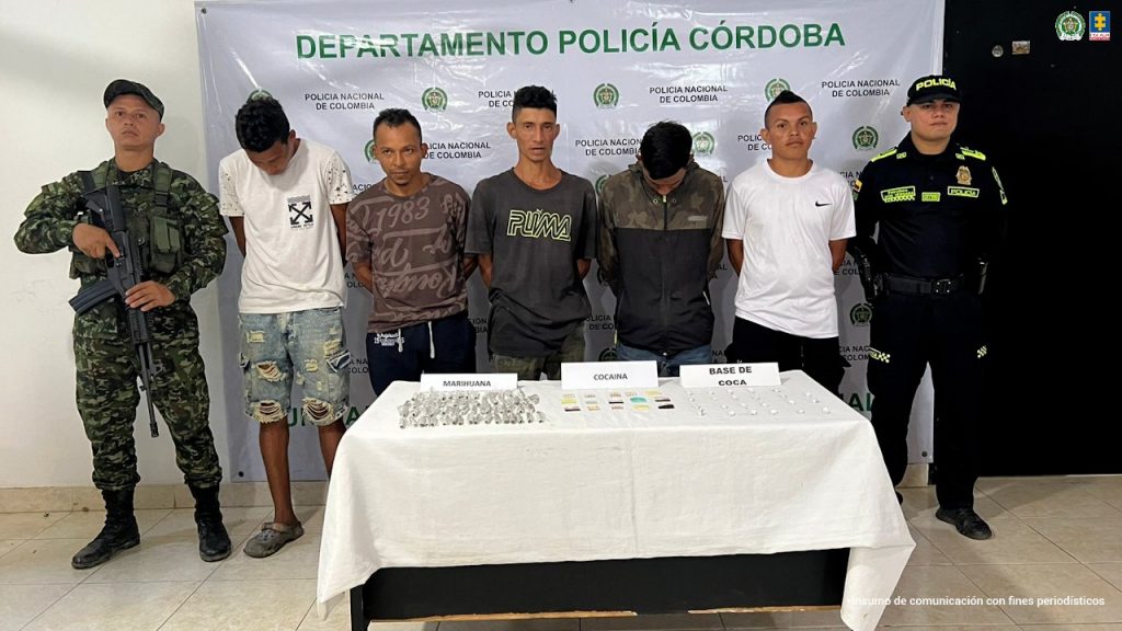 En la imagen aparecen cinco personas detenidas, entre dos uniformados de la Policía y frente a una mesa con alucinógenos.