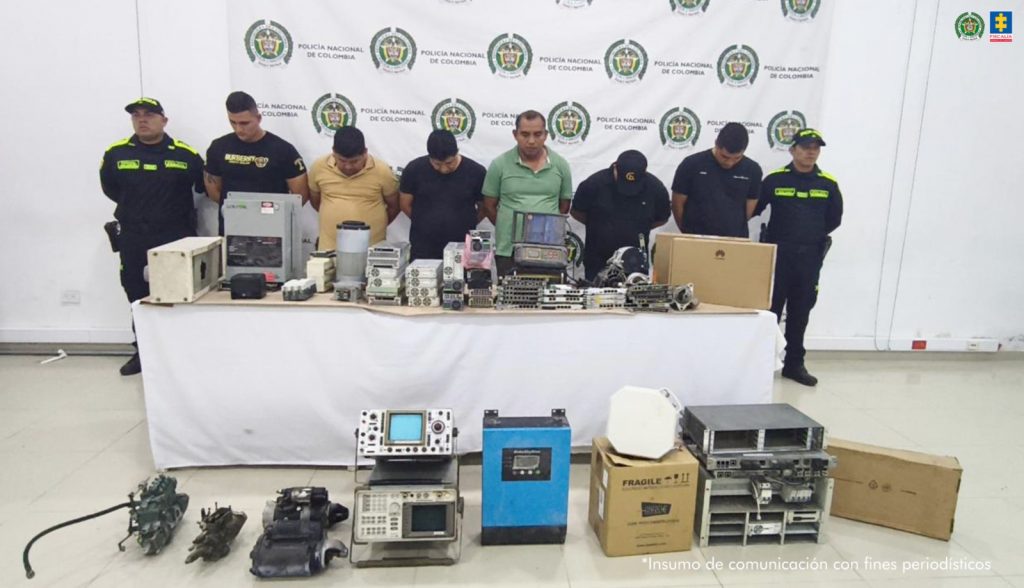 En la imagen aparecen seis personas detenidas, entre dos uniformados de la Policía Nacional y frente a una mesa con objetos electrónicos y otros insumos de telecomunicaciones.