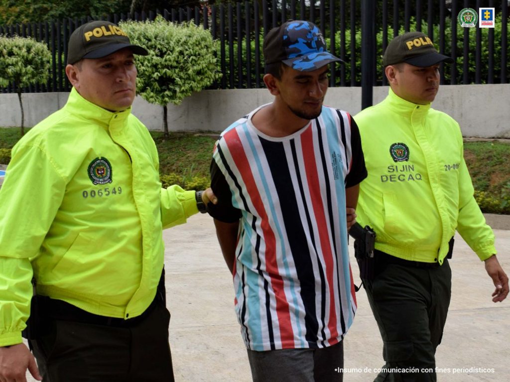 En la imagen se ve una persona detenida bajo custodia de dos integrantes de la Policía Nacional. Todos están caminando.