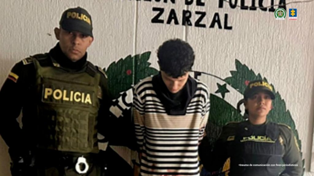 En la fotografía aparece de pie y con los brazos atrás Julián Andrés Arana Castrillón. Viste con buso con rayas horizontales de colores negro, y naranja. A sus extremos hay uniformados de la Policía Nacional. Detrás de ellos se aprecia parte del escudo de la Policía.
