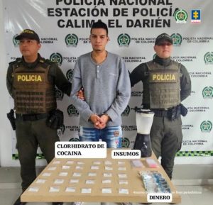 En la fotografía aparecen de pie y con los brazos atrás Anthonis Eloy Cortez Abache y Yeimi Manuel Freides Albornoz. Uno, viste con buso de color rojo y con estampado negro a la altura del pecho; así como pantalón oscuro. La otra persona viste con camisa de cuello blanco, mangas cortas de color negro y pantalón negro. En sus extremos hay uniformados de la Policía. Delante de ellos hay una superficie con mantel blanco y sobre ella se aprecian gran cantidad de bolsas pequeñas con contenido claro, rosado, vegetal y café. Detrás de ellos hay un pendón institucional de la Policía.