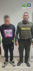 En la fotografía se aprecia de pie y con los brazos atrás a Julián Darío Rodríguez Ayala. Viste buso de manga larga, de color negro, con el estampado multicolor de una zapatilla, en la altura del pecho; asimismo, usa pantalón negro con estampado de la palabra ‘Nike’ en la parte inferior de la manga derecha; zapatillas en color blanco y negro. A su lado izquierdo hay un uniformado de la Policía Nacional.