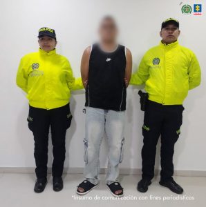 En la imagen aparece una persona de suéter negro y jean, entre dos uniformados de la Policía Nacional.