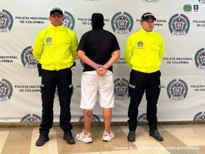 Se observa al detenido de espaldas, a cada lado un uniformado de Policía Nacional y atrás un pendón de la misma institución.