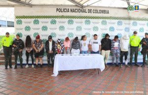 Se observan 11 personas capturadas, en fila y de frente. A ambos costados funcionarios de Policía Nacional. Atrás un pendón de Policía Nacional. Al frente una mesa con material incautado