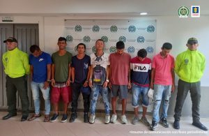 se observan siete capturados en fila.  En cada extremo un funcionario de Policía nacional. Al fondo el pendón de Policía Nacional.