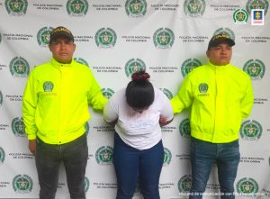En la imagen aparece una persona con camiseta blanca y jean, entre dos uniformados de la Policía.