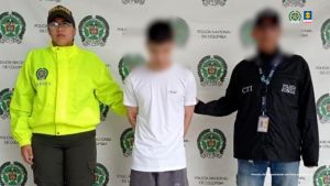 En la fotografía se aprecia de pie y con los brazos atrás a Kevin Alexánder Grisales Ordóñez. Viste camiseta blanca, de manga corta; bermuda de color gris y pantuflas azules. A su izquierda hay un servidor del CTI de la Fiscalía y a su derecha una uniformada de la Policía Nacional. Detrás de ellos hay un pendón institucional de la Policía.