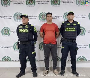 En la imagen aparece una persona de camiseta naranja y jean, entre dos uniformados de la Policía Nacional. 