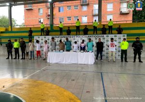 En la fotografía están los 11 procesados con varios servidores de la Policía Nacional y adelante una mesa con una subametralladora artesanal, 9 cartuchos, un silenciador y más de 550 dosis de marihuana y cocaína, incautados durante los allanamientos.