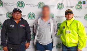 En la imagen aparece una persona de suéter gris entre dos funcionarios de la Policía y del CTI.