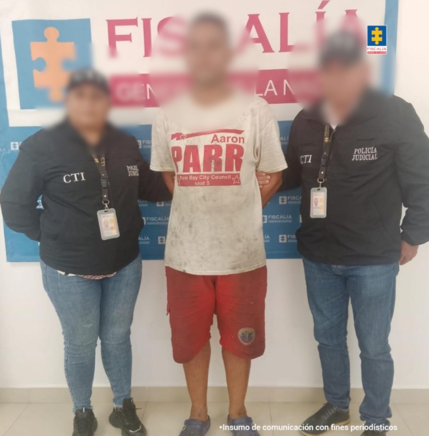 En la imagen aparece una persona de pantaloneta roja y suéter gris, entre dos uniformados del CTI.