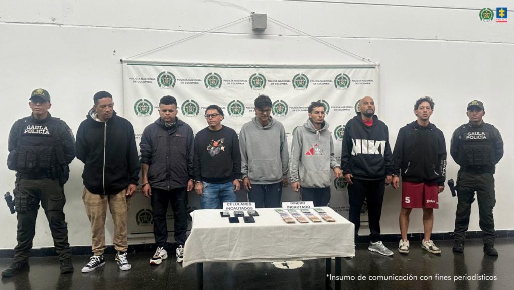 En la fotografía están los 7 procesados con un servidor del Gaula de la Policía y una mesa con 5 celulares y dinero, incautados durante el operativo de allanamiento y captura