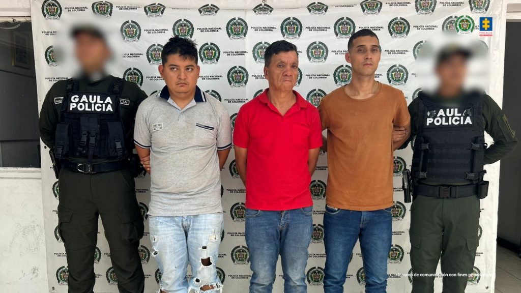 Los tres capturados se encuentran de frente y custodiados por dos uniformados del Gaula de la Policía Nacional. Detrás se observa un backing de la Policía Nacional.