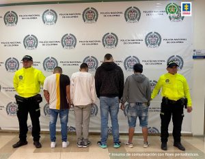 Se observan cuatro personas capturadas, todos de espaldas y en fila. En ambos costados funcionarios de Policía Nacional. Al fondo un pendón de Policía Nacional.