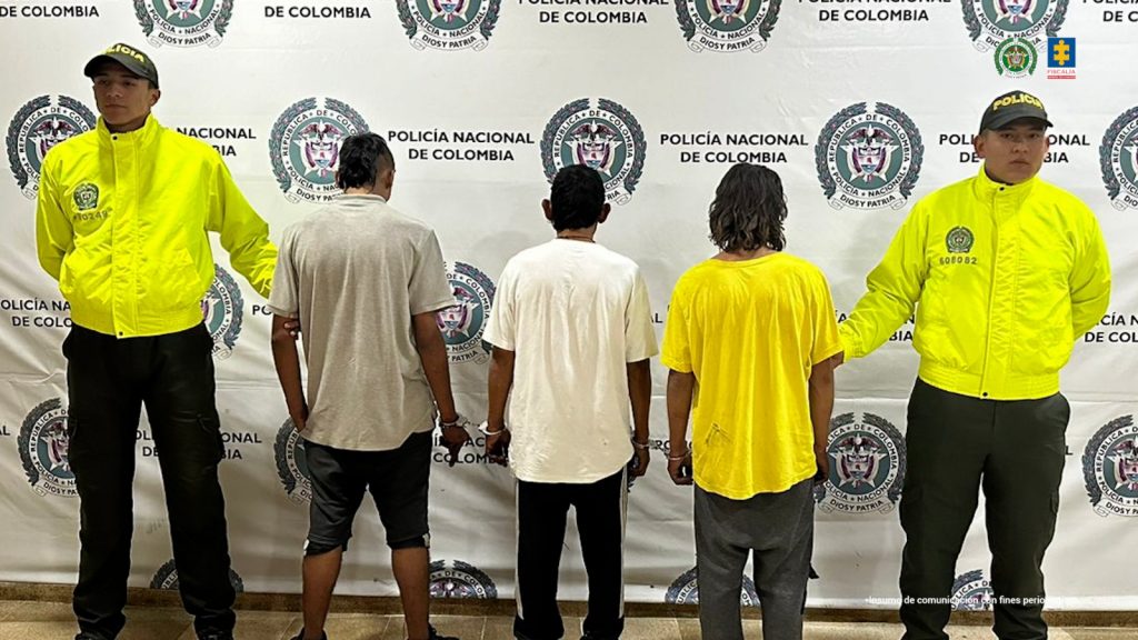 Se observan tres hombres en fila y de espaldas. A cada lado de la fila un uniformado de Policía Nacional. Atrás, un pendón de Policía Nacional.