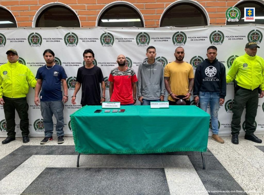 En la imagen se encuentran los 7 procesados con un pendón de la Policía Nacional al fondo y dos uniformados en ambos lados