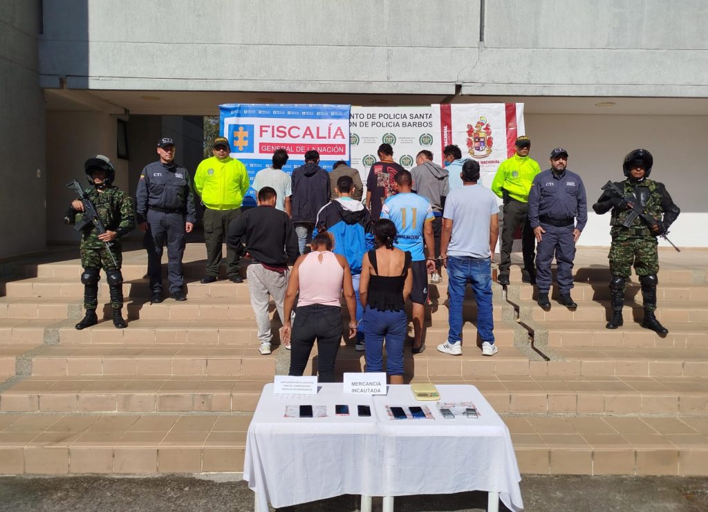 en la imagene se ve a los 12 detenidos de espaldas custodiados por agentes del CTI y la policia, detras de ellos hay un baking de la fiscalia y la policia