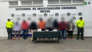 En la fotografía aparecen de pie y agachados los presuntos integrantes del grupo delincuencial La Alianza o La Playita. A lado y lado de ellos hay uniformados de la Policía Nacional. Delante de ellos hay una mesa con mantel verde y sobre ella varios elementos incautados como estupefacientes, dos armas de fuego y varios teléfonos celulares. Detrás de ellos hay un pendón institución de la Policía Nacional.