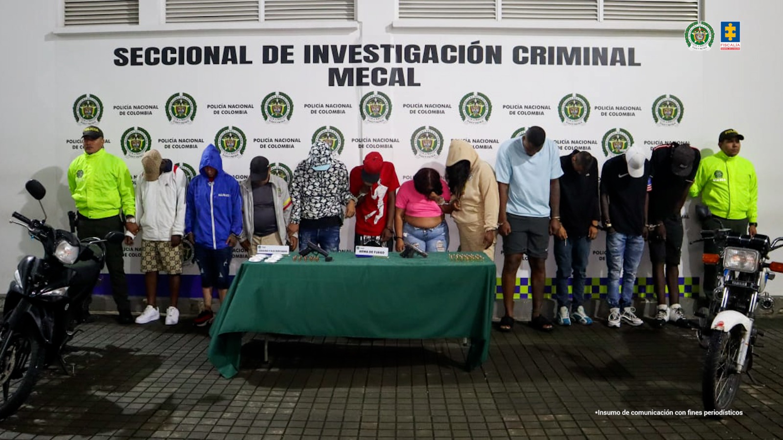 En la fotografía se aprecian de pie, en hilera y esposados entre sí a los 11 presuntos integrantes de ‘La Empresa’. A sus extremos hay uniformados de la Policía y dos motocicletas. Delante de ellos hay una mesa con mantel verde y sobre ella hay bolsas plásticas con contenido blanco, dos armas de fuego y munición. Detrás de ellos hay un pendón institucional de la Policía.